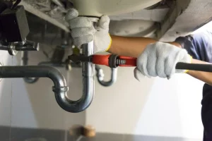 man with gloved hand and red wrench fixing pipes under counter