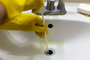 a yellow glove using the drain cleaner on a bathroom faucet