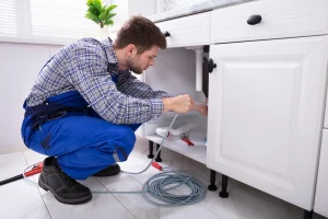 A man in overalls taking a look under a vanity sink