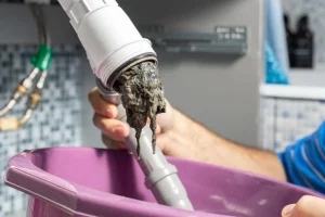 contents of a clogged drainage pipe going into a purple container