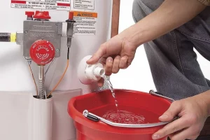 removing water from the water heater into a red bucket- water heater maintenance